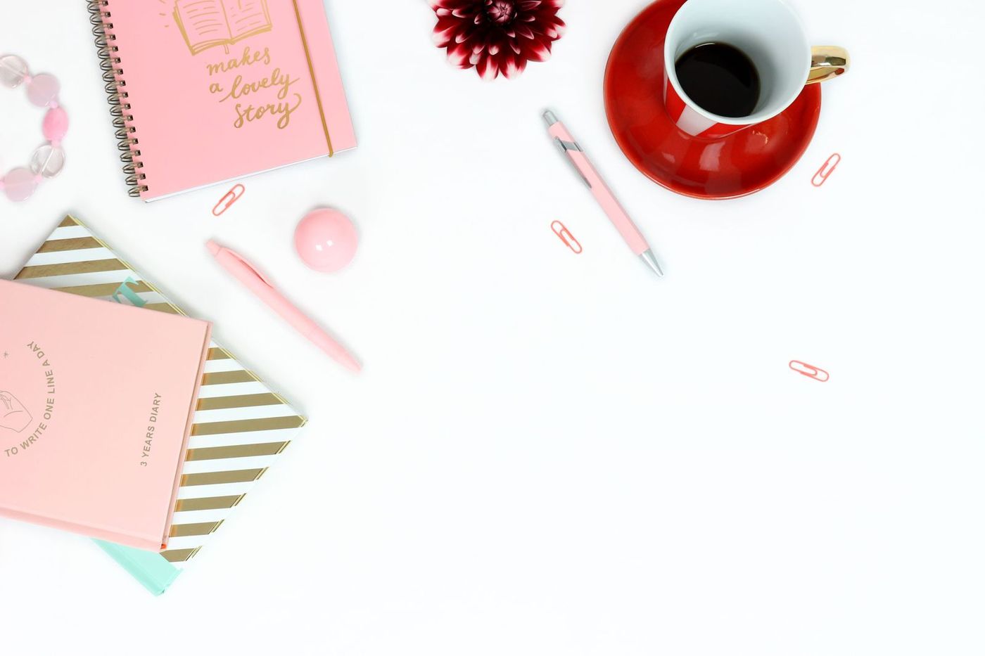 Roze notitieboekjes en een kop koffie op een wit bureau