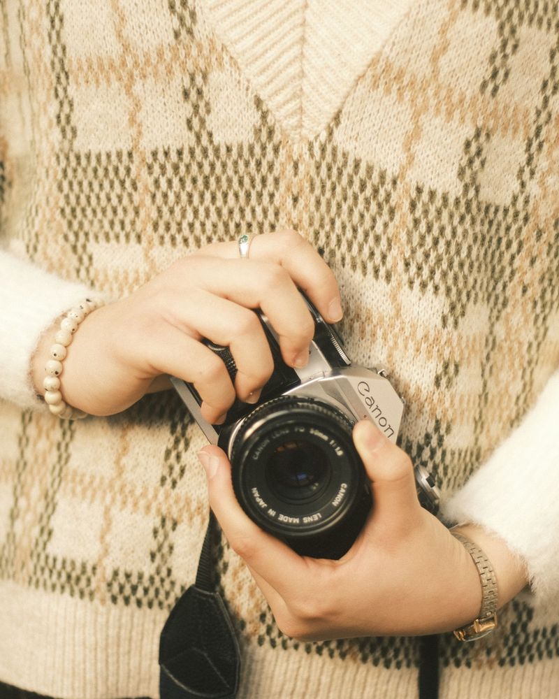 Handen met een camera, gebreide trui op de achtergrond